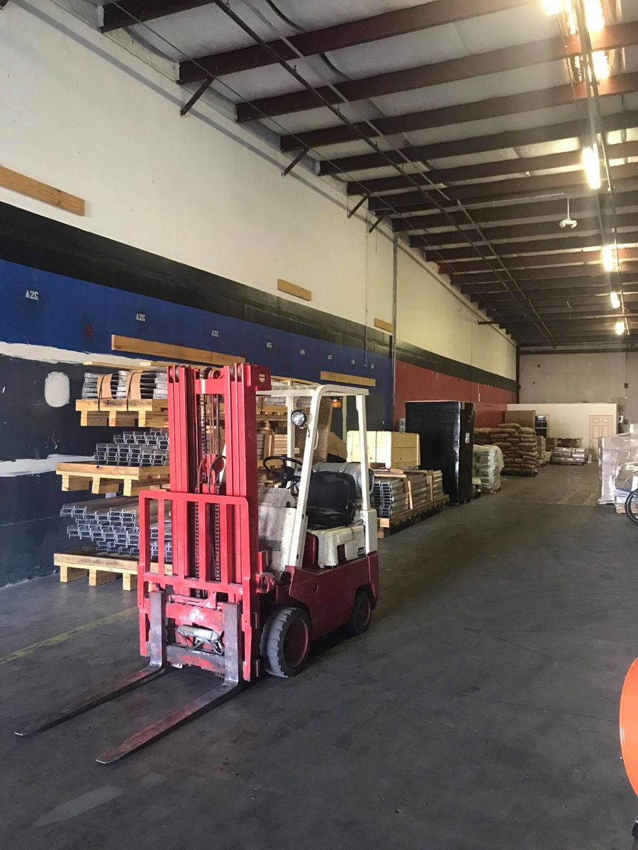 Warehouse aisle with a forklift, palletized merchandise and racks of metal profiles